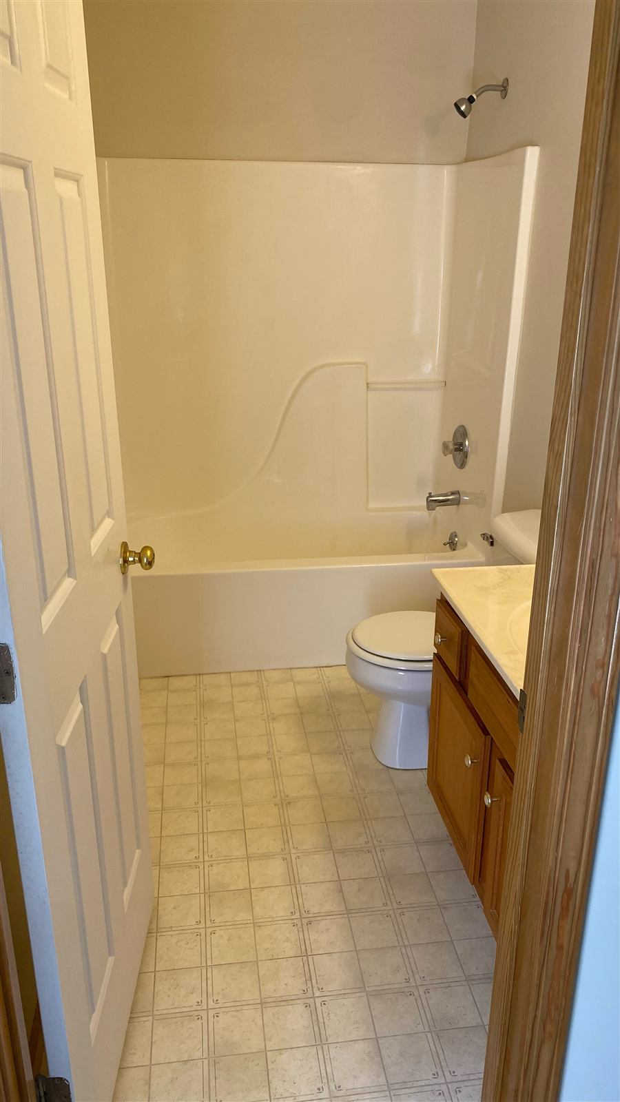 Dated bathroom before remodel with beige tub surround and oak vanity