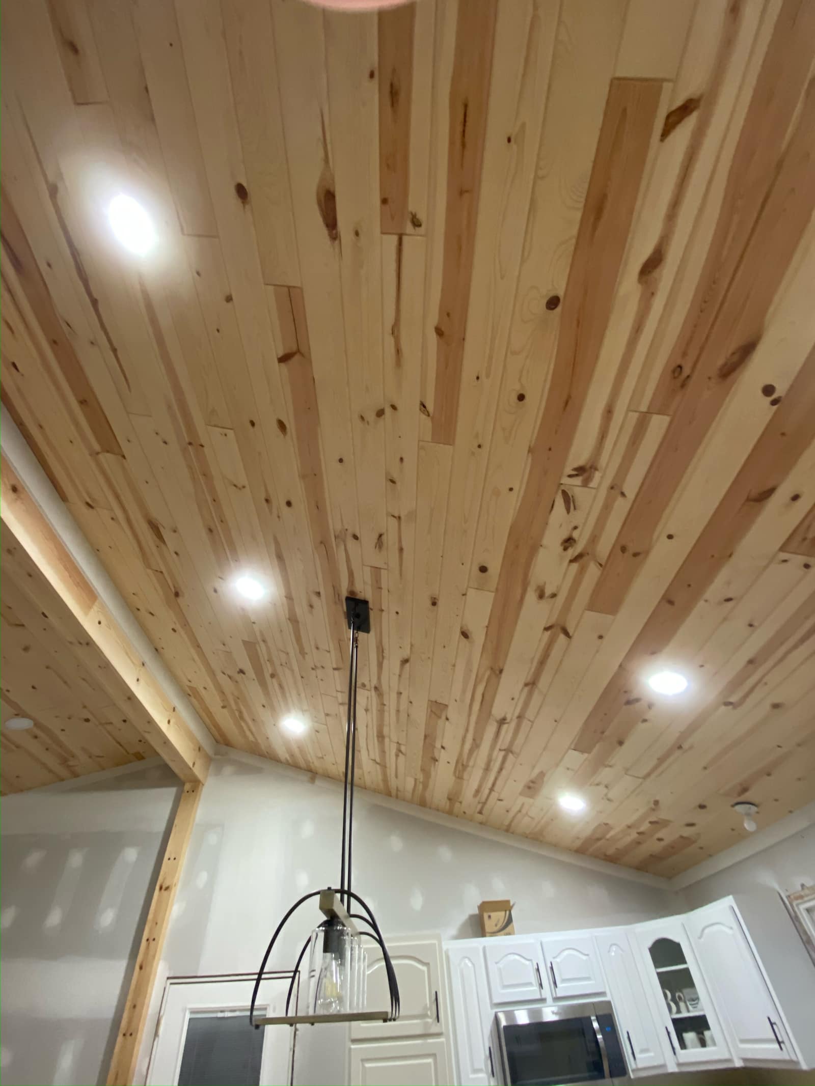 Vaulted tongue-and-groove pine ceiling with recessed lighting over a kitchen