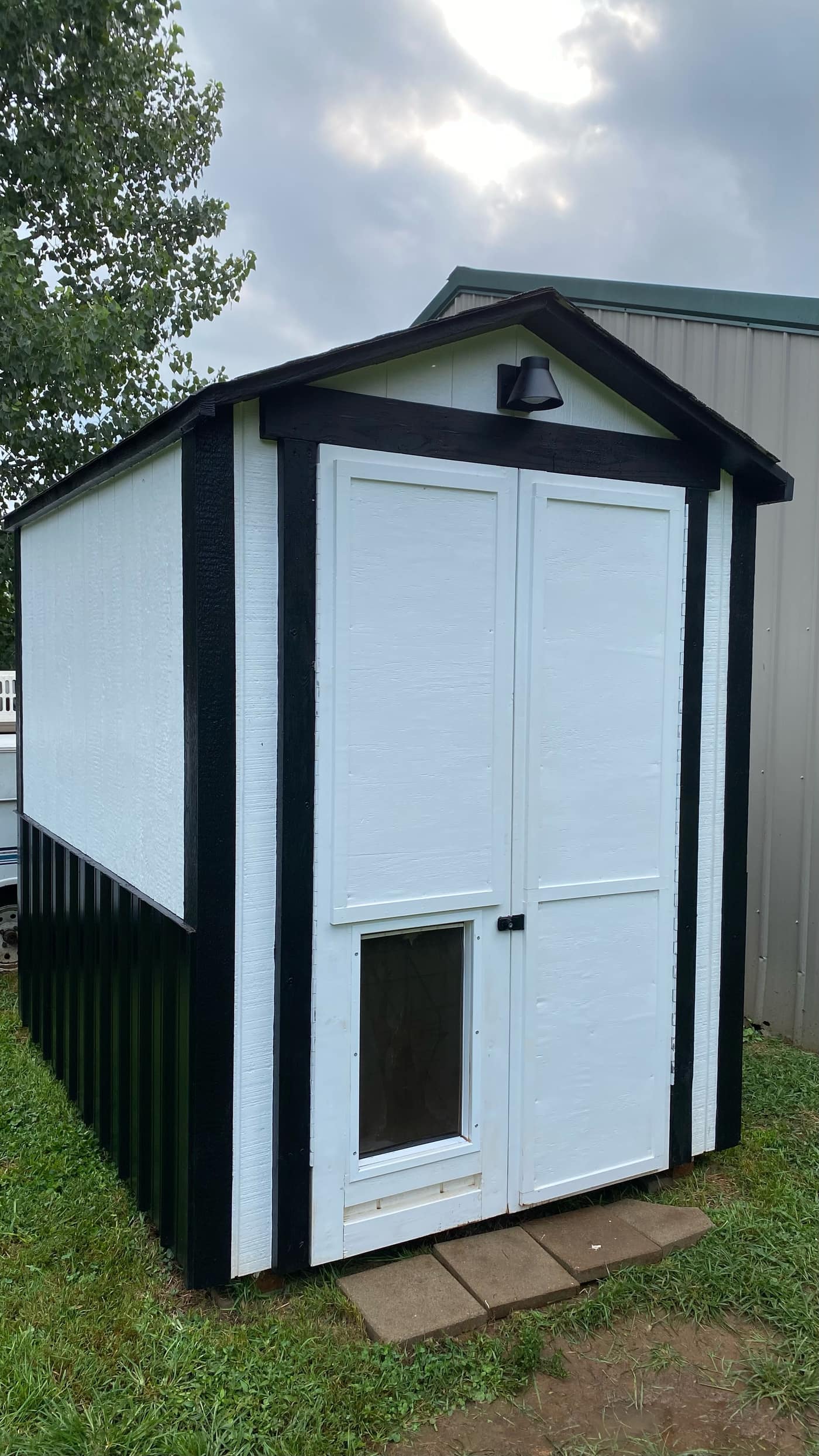 Rebuilt shed with fresh white siding, black trim, new doors, and exterior light