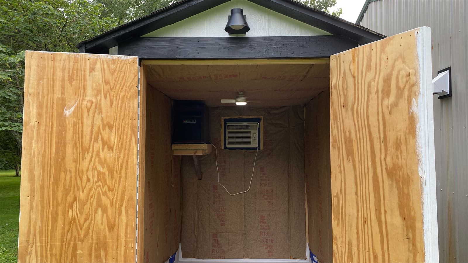 Shed interior with insulation, wiring, ceiling fan light, heater, and window AC installed