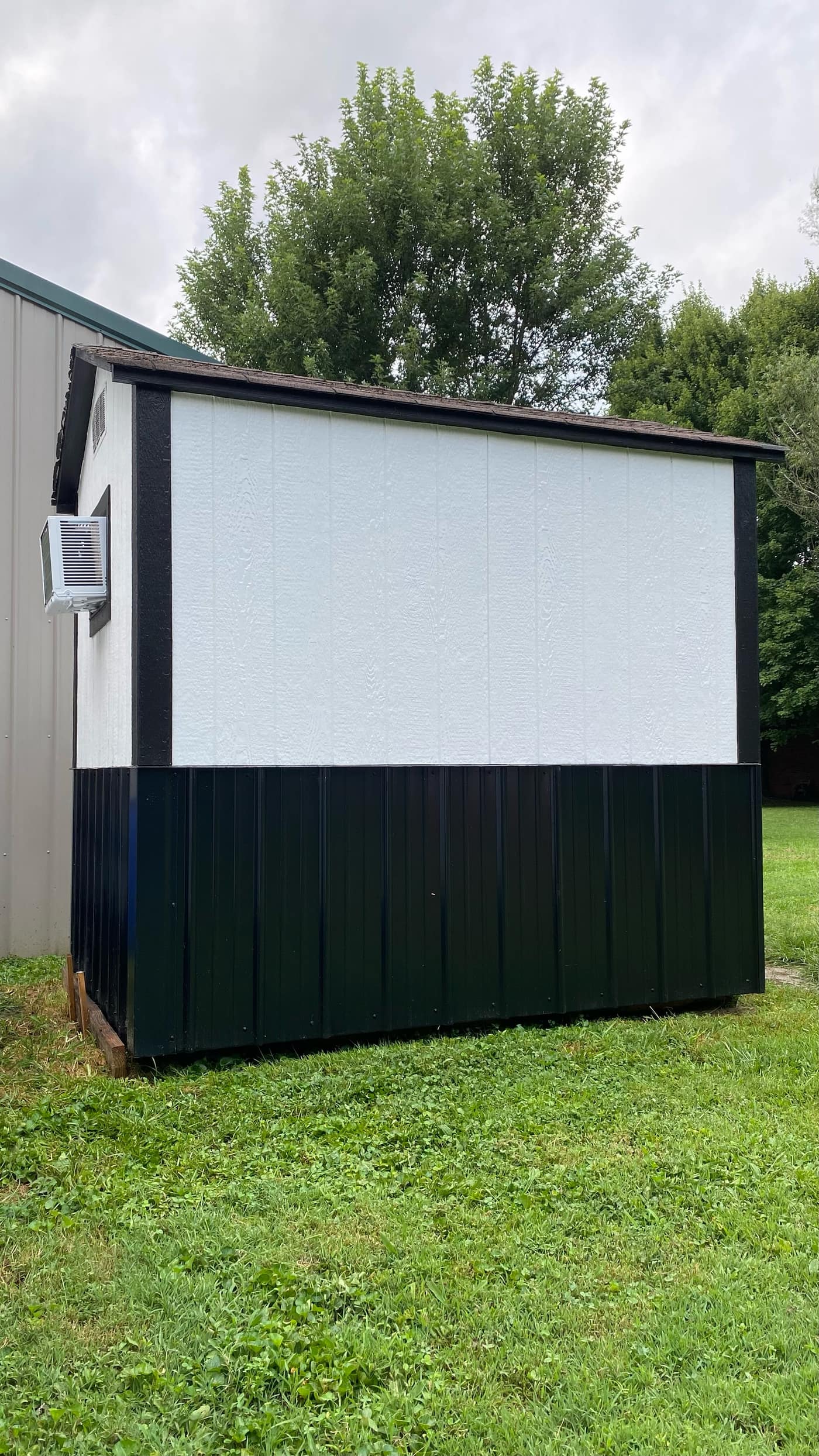 Side view of the rebuilt shed with white siding, black metal wainscot, and a window AC unit